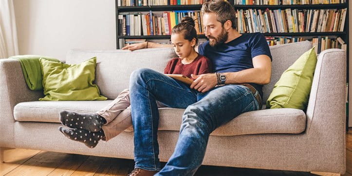 Il padre si si siede con la figlia sul divano e legge un libro