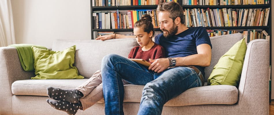 Father sits with daughter on the sofa and reads a book