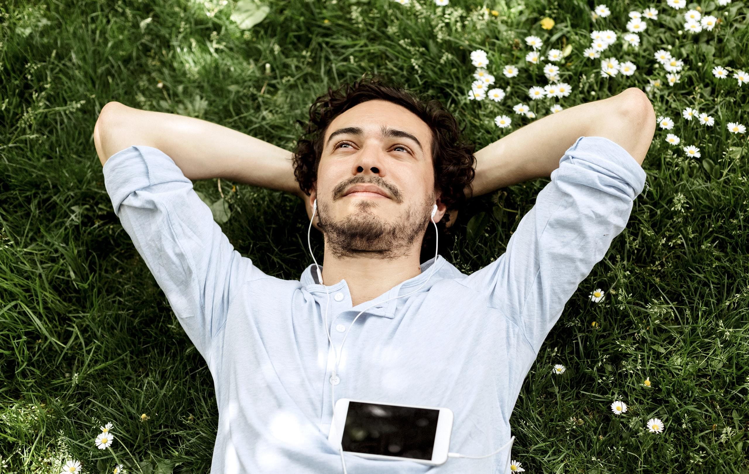 Man lies on meadow, looks into the sky and listens to music.