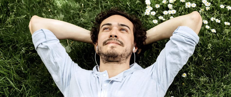 Man lies on meadow, looks into the sky and listens to music.