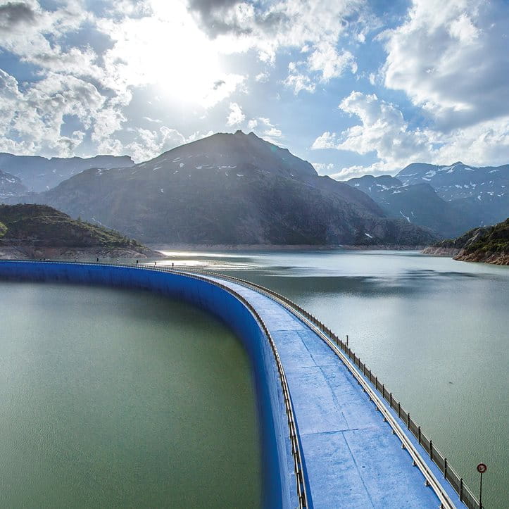 Un pont bleu au-dessus d'un lac entre un paysage de montagnes