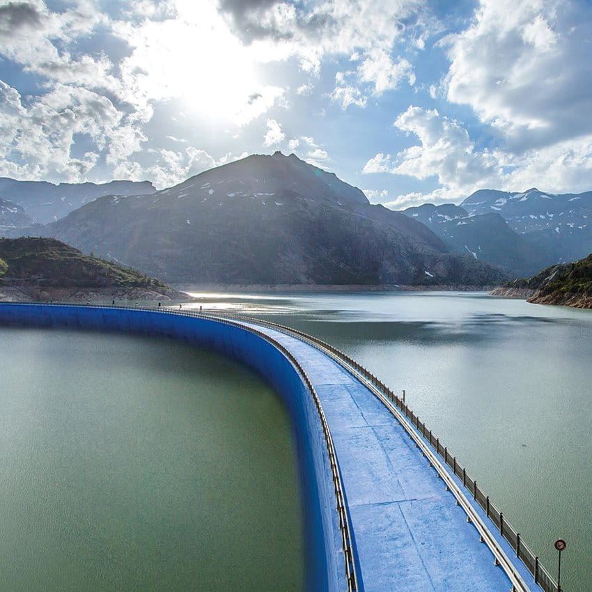A blue bridge over a lake between a mountain landscape