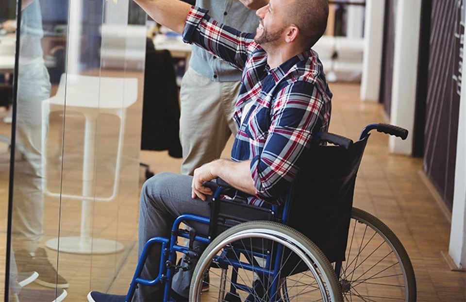 Un uomo in sedia a rotelle abbozza un'idea con il suo collega di lavoro su una parete di vetro dell'ufficio.