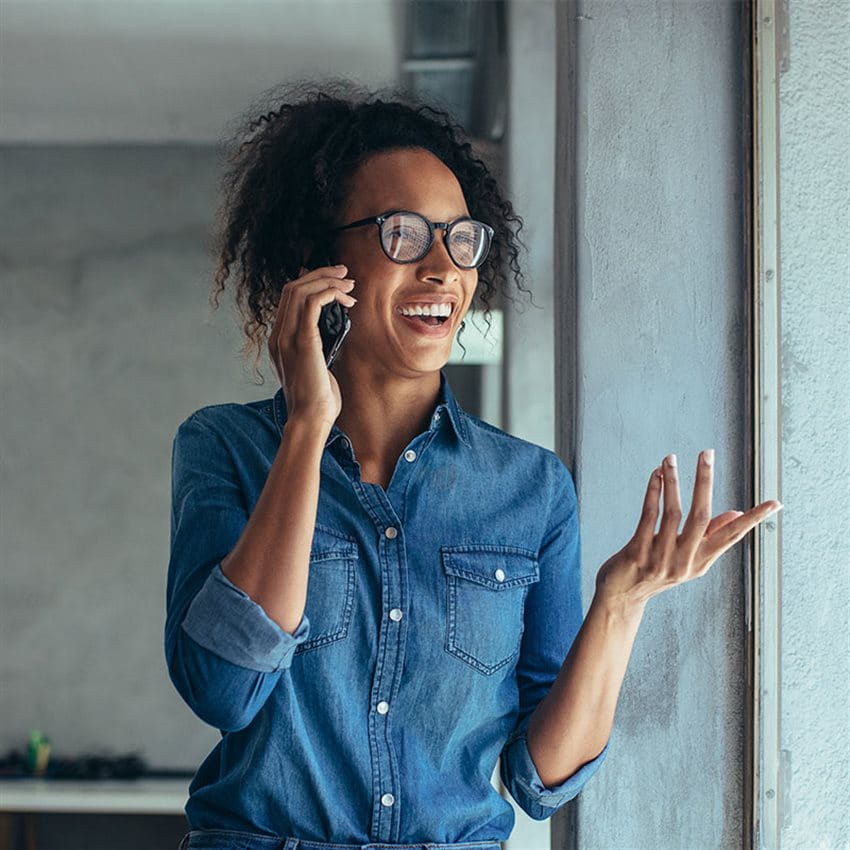 Eine Frau in blauem Jeans-Hemd telefoniert mit ihrem Mobile-Telefon und spricht über Ihre positive Erfahrung mit der Online-Versicherung der Zurich Versicherung.