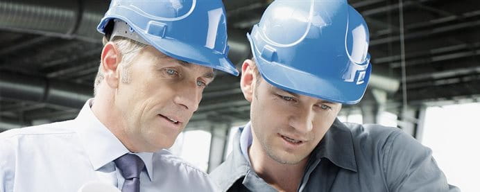 Two men with helmets talking at a construction site.