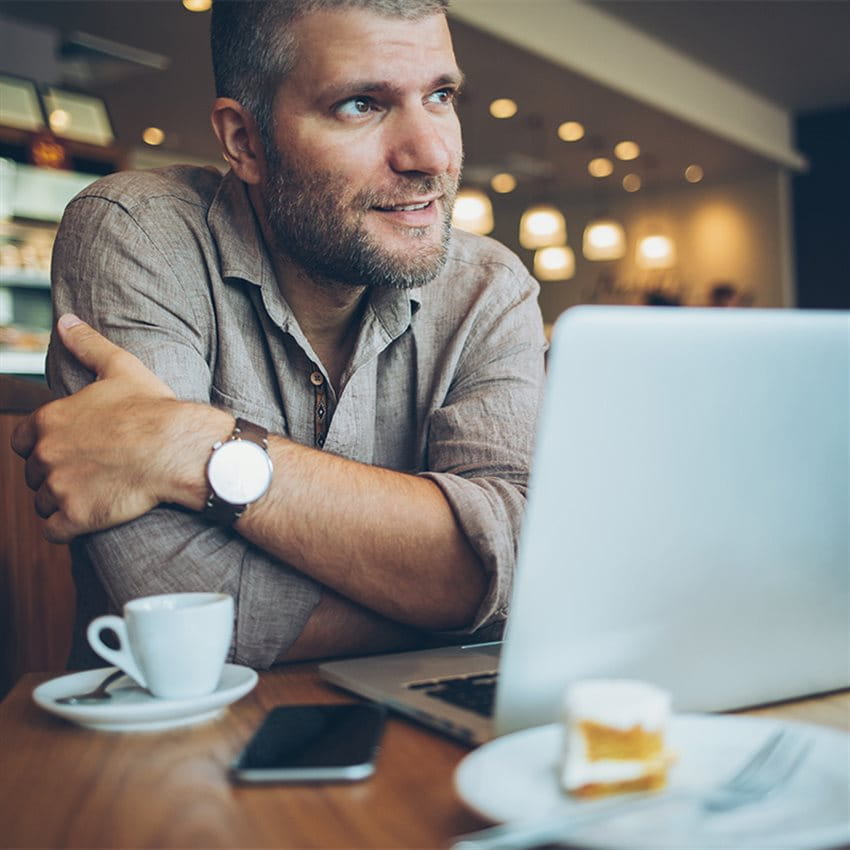 Mann vor einem Laptop in einer Kaffeebar.