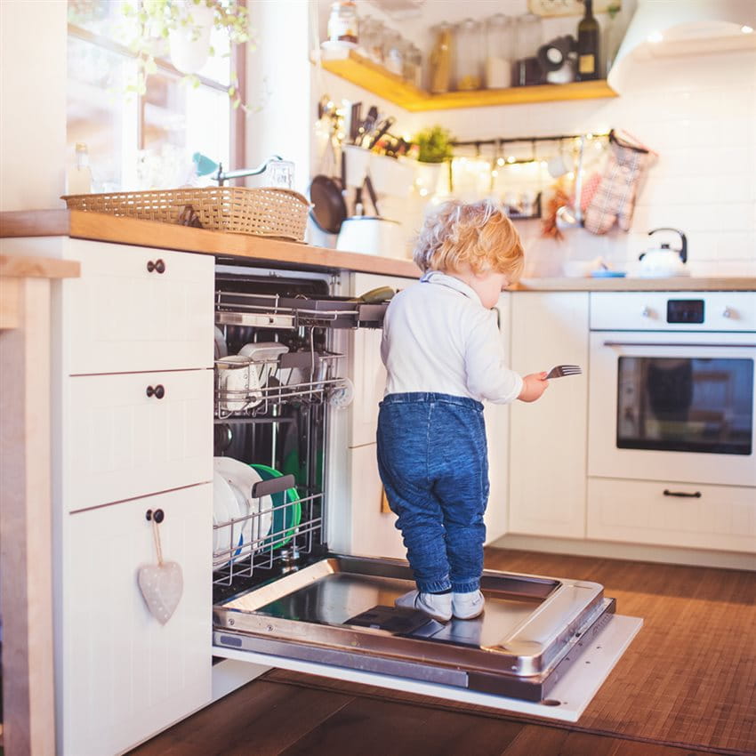 Ein Kind steht auf der Abwaschmaschinen Türe