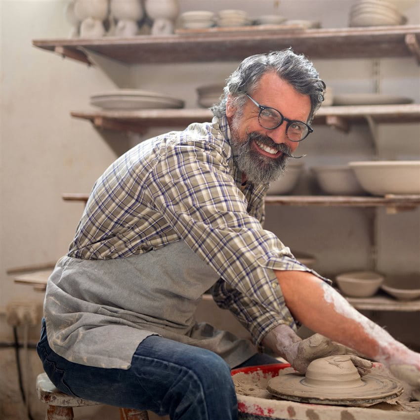 Male potter molding clay with a smile