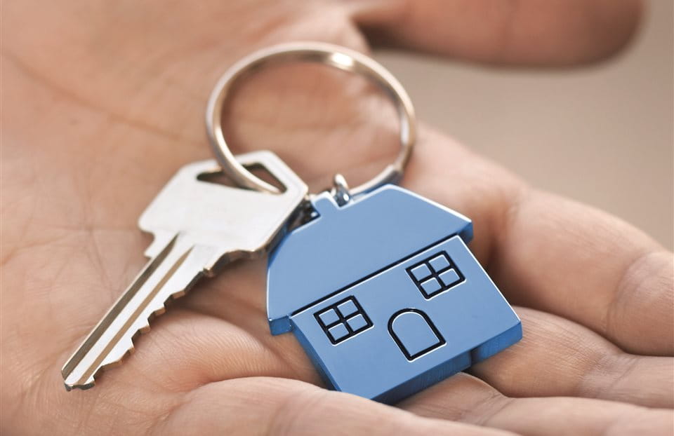 Hand mit Schlüssel und blauem Haus-Schlüsselanhänger in der Hand