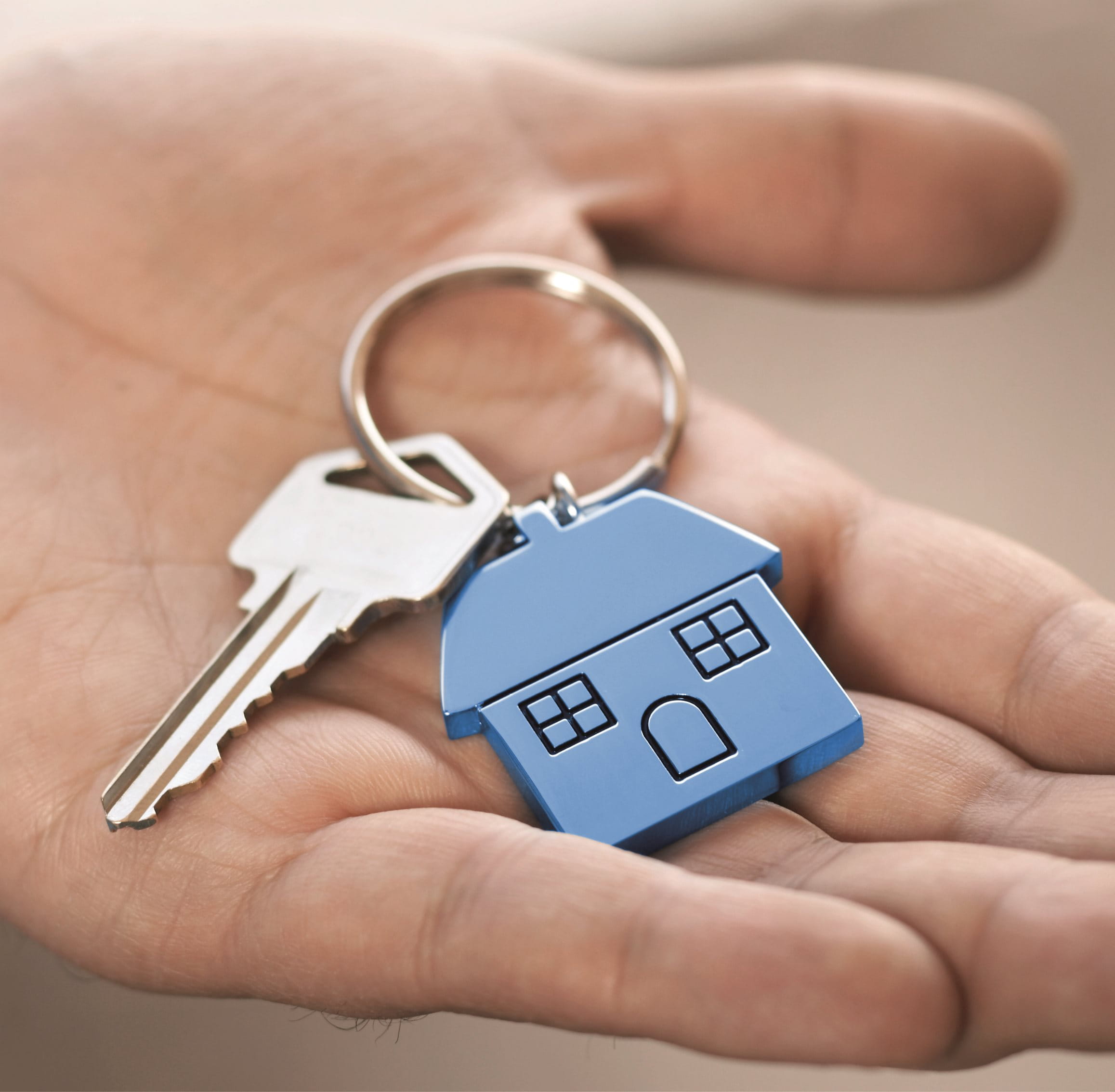 Hand mit Schlüssel und blauem Haus-Schlüsselanhänger in der Hand