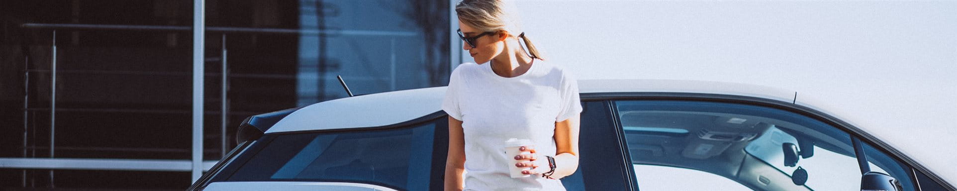  Woman stands in front of her car at the electric charging station and drinks coffee