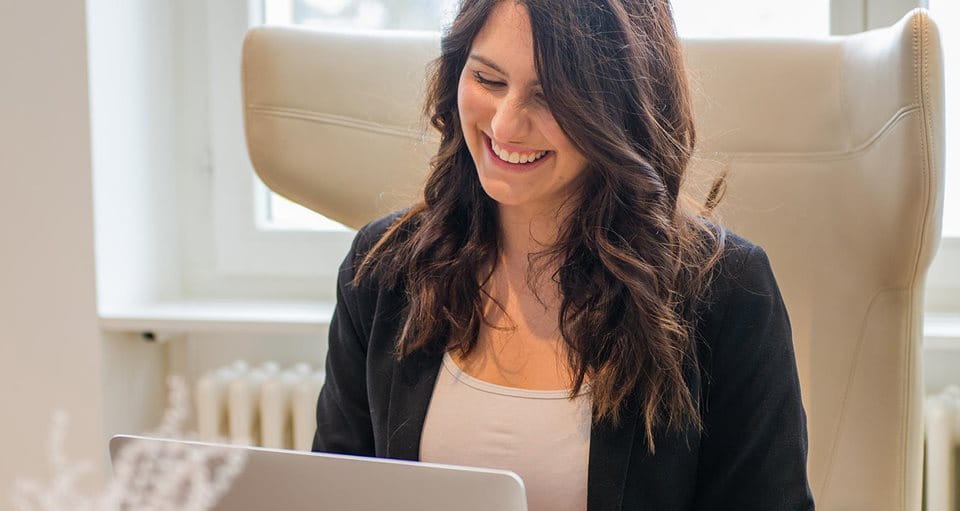 Jeune femme assise devant un ordinateur portable et riant