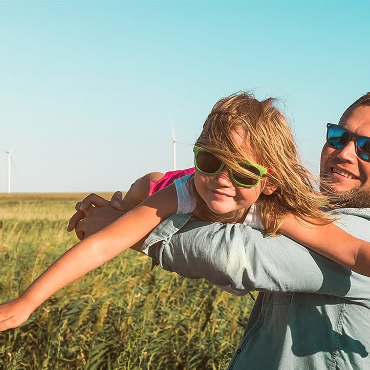 Man with child in a field in front of wind turbines