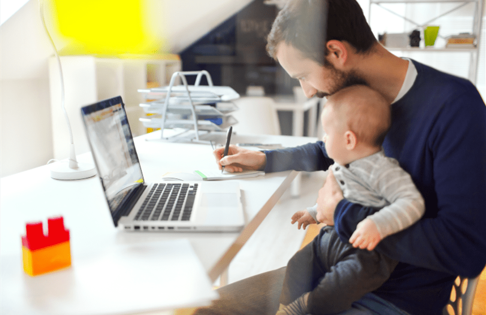 Un père est assis devant son ordinateur avec son bébé