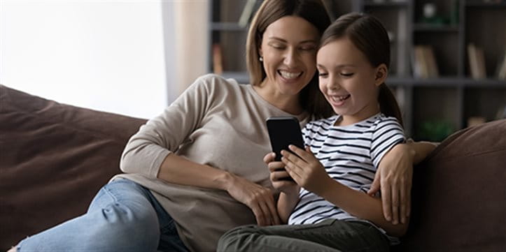 Mother sits with her daughter on the sofa and looks at a smartphone.