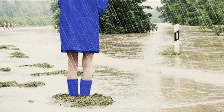 Frau steht mit Regenjacke und Gummistiefel im Hochwasser
