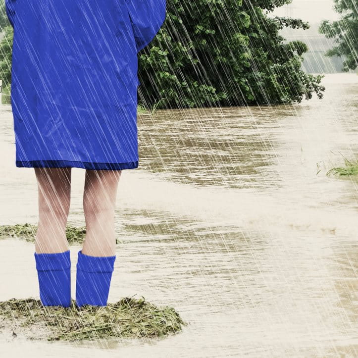 Woman standing in a flood wearing a raincoat and rubber boots
