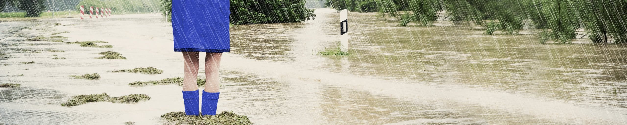 Frau steht mit Regenjacke und Gummistiefel im Hochwasser