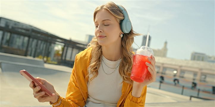 Una giovane ragazza ascolta musica tramite cuffie e tiene in mano una bevanda al tè freddo