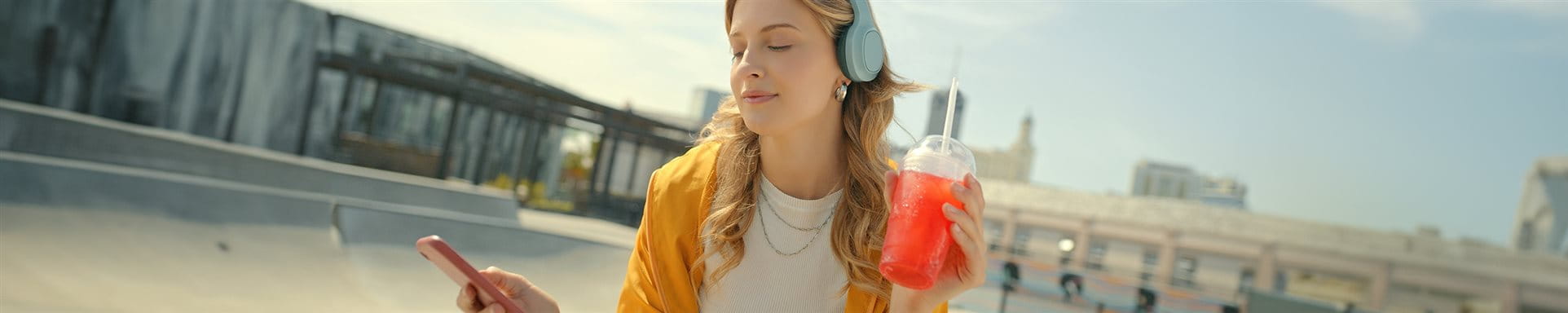 Young girl listens to music through headphones and holds an icetea.