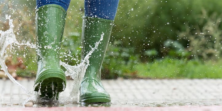 Woman jumps into puddle in green wellies