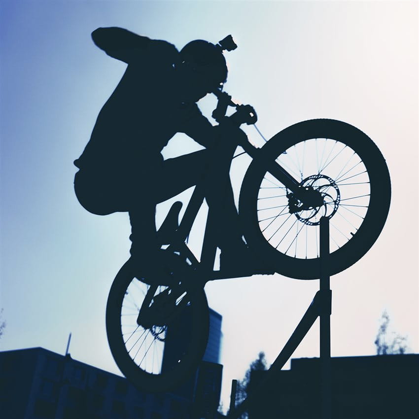 BMX-Fahrer mit Helmkamera im Gegenlicht beim Springen über Hindernis
