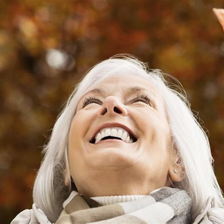 Una donna butta sorridendo delle foglie secche in aria.